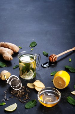 Çay nane, limon, limon ve zencefil karanlık bir arka plan üzerinde. Çay, kıyılmış zencefil kökü gibi için malzemeler yanında nane yaprakları, dilim limon ve kireç. İlaç ve ilaç kullanmaya gerek kalmadan soğuk algınlığı tedavisinde kavramı