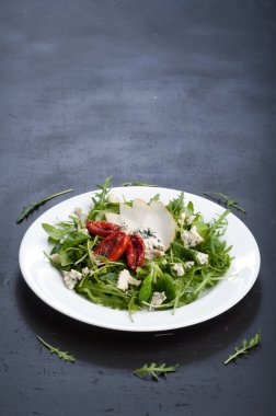 The concept of Italian food. Salad with arugula, pear slices, dried tomatoes and blue cheese on dark board. Vegetarian ready meal