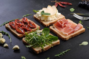 The concept of Italian food. Sandwiches with various fillings, such as arugula, dried tomatoes, pear, blue cheese and ham on dark background