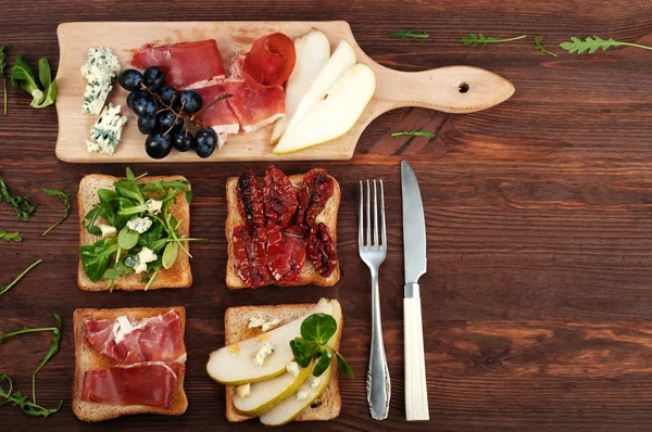 Sandwiches with various fillings, such as arugula, dried tomatoes, pear, blue cheese and ham on wooden background