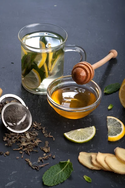 Té con menta, lima, limón y jengibre sobre un fondo oscuro. Además de los ingredientes para el té, como raíz de jengibre picada, hojas de menta, rodajas de limón y lima. El concepto de tratamiento de los resfriados, sin el uso de píldoras y medicamentos — Foto de Stock