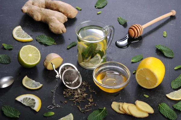 Té con menta, lima, limón y jengibre sobre un fondo oscuro. Además de los ingredientes para el té, como raíz de jengibre picada, hojas de menta, rodajas de limón y lima. El concepto de tratamiento de los resfriados, sin el uso de píldoras y medicamentos — Foto de Stock