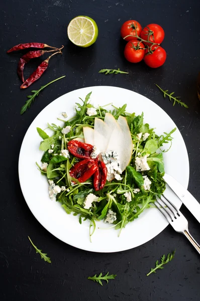 The concept of Italian food. Salad with arugula, pear slices, dried tomatoes and blue cheese on dark board. Vegetarian ready meal — Stockfoto