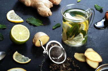 Ginger tea with lemon, lime and mint on black background. Beside the ingredients for tea, the same as the mint leaves, chopped ginger root, slices of lemon and lime. The concept of treatment of colds folk methods.