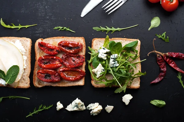 The concept of Italian food. Sandwiches with various fillings on a dark background. Sandwiches with pears, arugula and blue cheese — Stockfoto