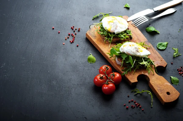 Sandwiches with arugula and poached egg on a wooden board. Near tomatoes and spices. The concept of useful home-made snacks — 스톡 사진