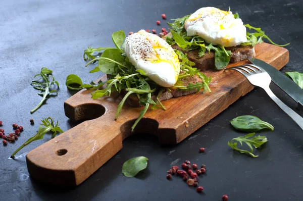 Sandwiches with arugula and poached egg on a wooden board. The concept of useful home-made snacks — 스톡 사진