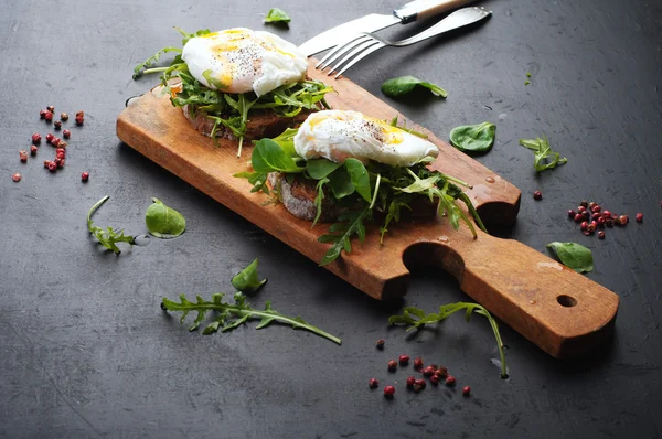 Panini con rucola e uovo in camicia su una tavola di legno. Il concetto di utili spuntini fatti in casa — Foto Stock