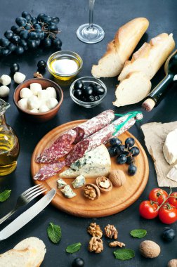 Italian food concept. Jerked sausage, various cheeses, blue grapes, vegetables and fruits on a dark background.