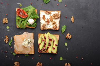 Roka, kurutulmuş domates, peynir, mavi peynir, fındık ve karanlık bir arka plan üzerinde avokado gibi Topingler çeşitli sandviçler. Sağlıklı Vejetaryen yiyecekler kavramı.