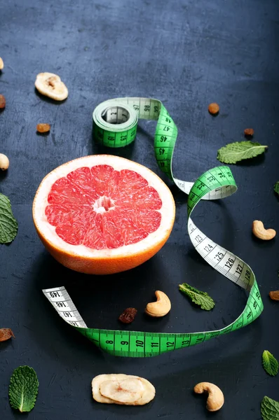 Classical diet. Half of grapefruit  on a dark background. Next measuring tape symbolizing decrease in volume of the body through proper balanced diet. Place for writing text or a prescription diet. — Stockfoto