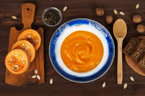 Σούπα κρέμα κολοκύθας σε ξύλινα φόντο, δίπλα από τα συστατικά για την παραγωγή σούπα. Η έννοια της ένα μενού για χορτοφάγους — Φωτογραφία Αρχείου