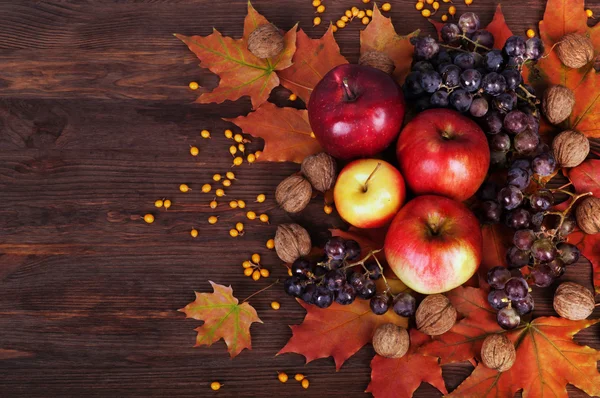 Fundo de outono. Maçãs, uvas, nozes e folhas amarelas sobre um fundo de madeira escura. Lugar para escrever texto ou receita . — Fotografia de Stock