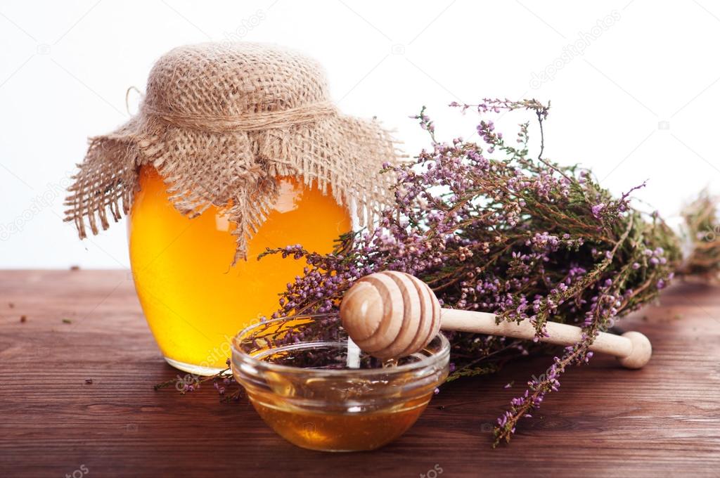 Honey in a glass jar near heather and spoon. White background.