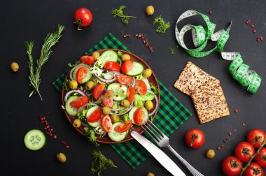 Concept diet food. Salad of fresh vegetables such as lettuce, purple onion, olives, cucumbers and tomatoes on a dark background. Vegetarian healthy dish