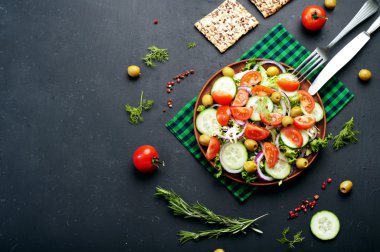 Concept diet food. Salad of fresh vegetables such as lettuce, purple onion, olives, cucumbers and tomatoes on a dark background. Vegetarian healthy dish