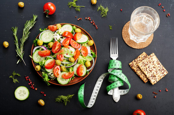 Concept diet food. Salad of fresh vegetables such as lettuce, purple onion, olives, cucumbers and tomatoes on a dark background. Vegetarian healthy dish