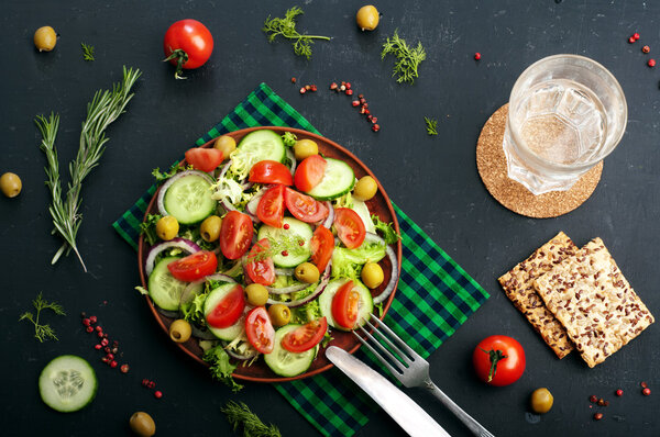 Concept diet food. Salad of fresh vegetables such as lettuce, purple onion, olives, cucumbers and tomatoes on a dark background. Vegetarian healthy dish