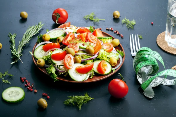 Concept diet food. Salad of fresh vegetables such as lettuce, purple onion, olives, cucumbers and tomatoes on a dark background. Vegetarian healthy dish — Stock Fotó