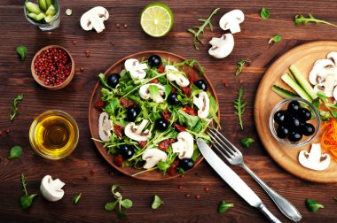 Salad with arugula, leaf mash, olives, sun-dried tomatoes and raw mushrooms. The concept of diet vegetarian food homemade
