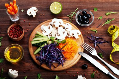 The concept of dietetic vegetarian food. Bright juicy shredded vegetables, such as carrots, purple cabbage, mushrooms and cucumbers, which lies on a circular wooden cutting board. Natural organic products, ready to eat