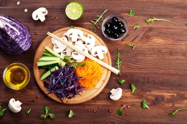 The concept of dietetic vegetarian food. Bright juicy shredded vegetables, such as carrots, purple cabbage, mushrooms and cucumbers, which lies on a circular wooden cutting board. Natural organic products, ready to eat — Stock Photo, Image