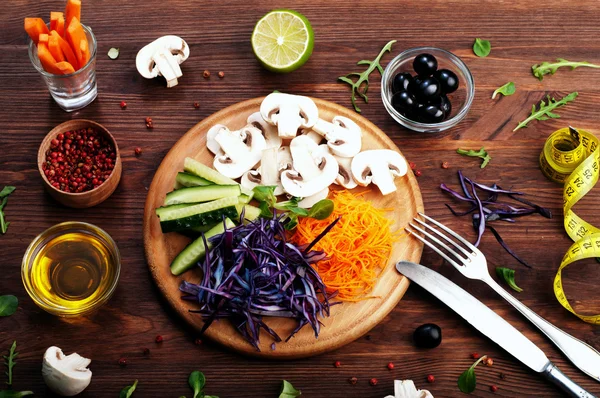 Le concept de nourriture végétarienne diététique. Légumes râpés juteux lumineux, tels que les carottes, le chou violet, les champignons et les concombres, qui se trouve sur une planche à découper circulaire en bois. Produits biologiques naturels, prêts à manger — Photo