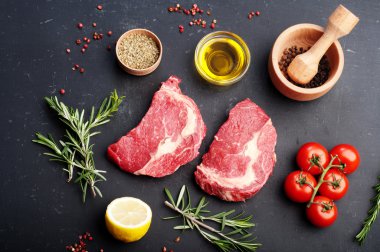 Çiğ dana eti biftek pişirmek için hazırlanmıştır. Biftek, baharat ve otlar pişirmek için malzemeler yanında.