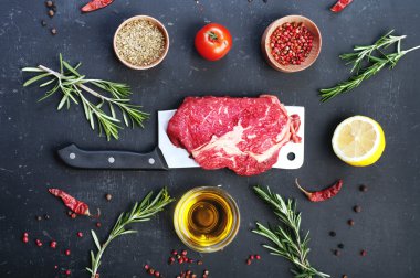 Kesme bıçağının üzerinde yatan çiğ biftek. Çiğ dana eti biftek pişirmek için hazırlanmıştır. Biftek, baharat ve otlar pişirmek için malzemeler yanında.