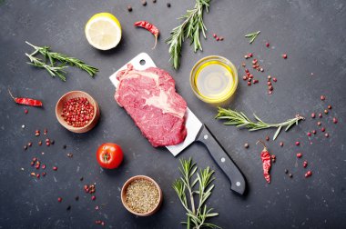 Kesme bıçağının üzerinde yatan çiğ biftek. Çiğ dana eti biftek pişirmek için hazırlanmıştır. Biftek, baharat ve otlar pişirmek için malzemeler yanında.