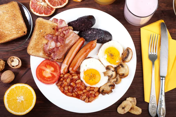 O café da manhã clássico inglês com ovos fritos, salsichas, pudim preto, cogumelos fritos e feijão com tomates em um fundo de madeira marrom. O conceito de um café da manhã saudável . — Fotografia de Stock