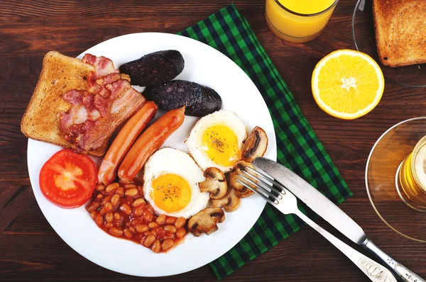 Het klassieke Engelse ontbijt met gebakken eieren, worstjes, bloedworst, gebakken champignons en bonen met tomaten op een bruine houten achtergrond. Het concept van een gezond ontbijt. — Stockfoto