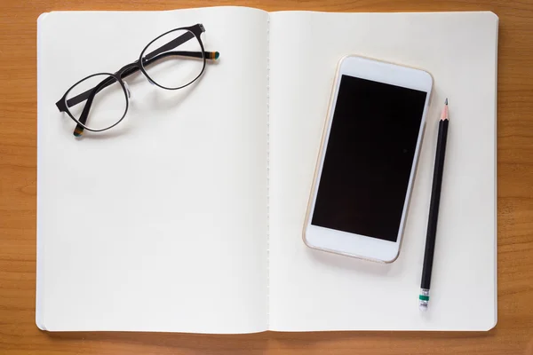 Teléfono celular, anteojos y lápiz en cuaderno blanco — Foto de Stock