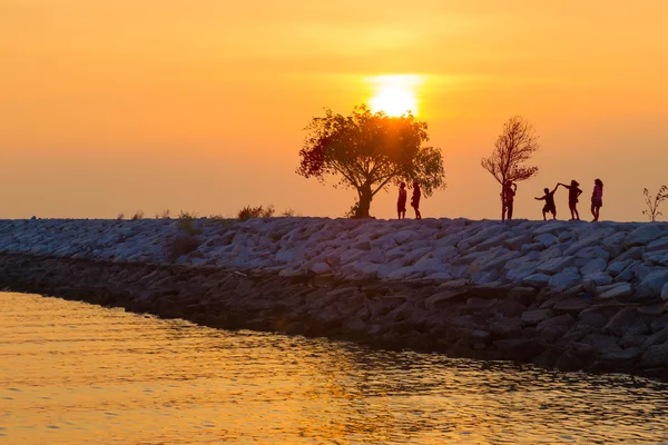 Silhouette insanlar ve güneşler sırasında kayalık bir iskelede küçük ağaçlar — Stok fotoğraf