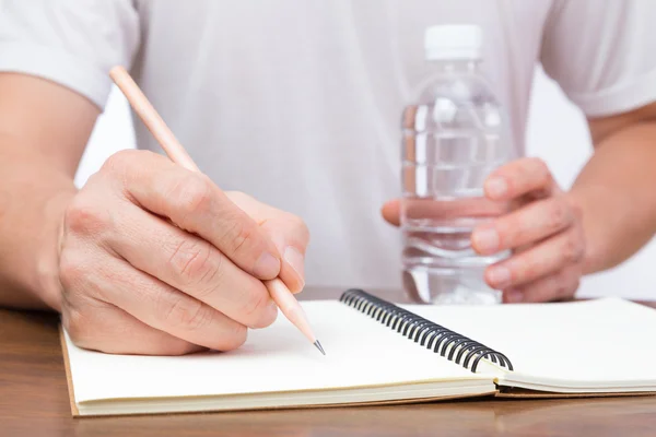 Homem escrevendo no caderno e segurando garrafa de água — Fotografia de Stock