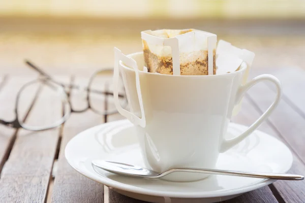 Coffee cup with packaged coffee on wooded table, blurred eyeglas