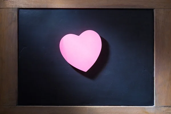 Pink hearted shape post-it note on blackboard — Stock Photo, Image