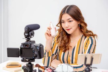 Güzel Asyalı genç bir kadın, vlogger, Prduct şişe tutuyor ve evdeki video blogu için güzellik ürünlerini internetten inceliyor.