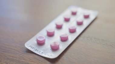 Ahşap masadaki pembe hapların kapağı bir erkeğin eliyle alınıyor.