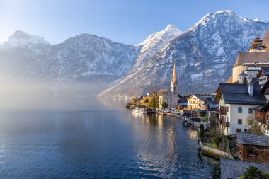 Güzel Hallstatt Gölü ve ünlü kilisenin manzarası ilkbaharın erken saatlerinde sabah erken saatlerde, dağ sıraları karla kaplanmış.