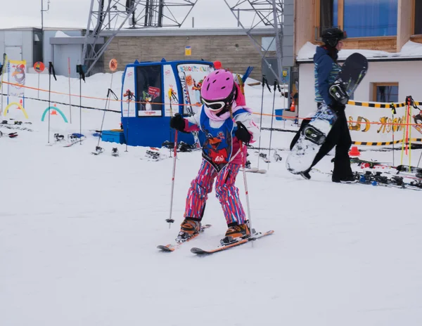 Liten flicka i en vacker flerfärgad ski suit, hjälm och skyddsglasögon är skidåkning. Österrike, Zams 22 Feb 2015 — Stockfoto