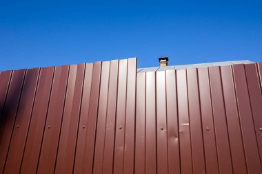 Mavi gökyüzüne karşı profil çizilmiş metal levhadan yapılmış bir çit. Soyut sanat fotoğrafçılığı.