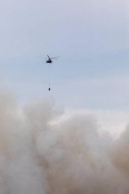 Yangın yüzünden dumanlı bir su tankı olan itfaiye helikopteri. Büyük bir yangından çıkan dumanlar..