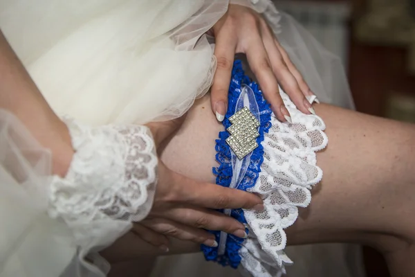 Невеста одевает подвязки на ногу. Фото красивых женских босых ног в свадебном платье. Невеста одевает чулки на ноги . — стоковое фото