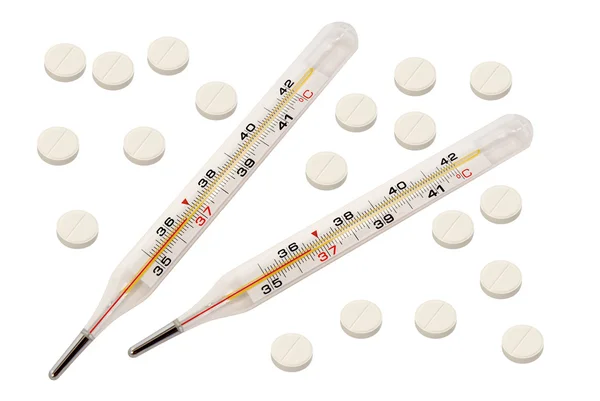 Két orvosi hőmérők és a sok szétszórt tabletta. Elszigetelt fehér háttér. — Stock Fotó