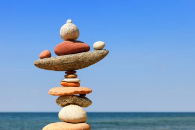 Denizin arka planındaki kumsalda renkli çakıl taşlarından oluşan bir taş zen piramidi. Yaşam dengesi, uyum ve meditasyon kavramı