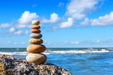 Yaz denizinin arka planında renkli çakıl taşı piramidi ve Cumulus bulutlarıyla mavi gökyüzü. Uyum, denge ve meditasyon kavramı.