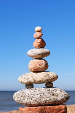 Dengeli taşlardan oluşan Rock zen Piramidi deniz ve mavi gökyüzünün arka planına karşı. Denge, uyum ve meditasyon kavramı