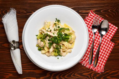 Brokolili makarna ve siyah ahşap bir masada beyaz tabakta tavuk. Üst görünüm