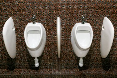 Erkekler tuvaletinde kahverengi arka planda beyaz pisuarlar var.